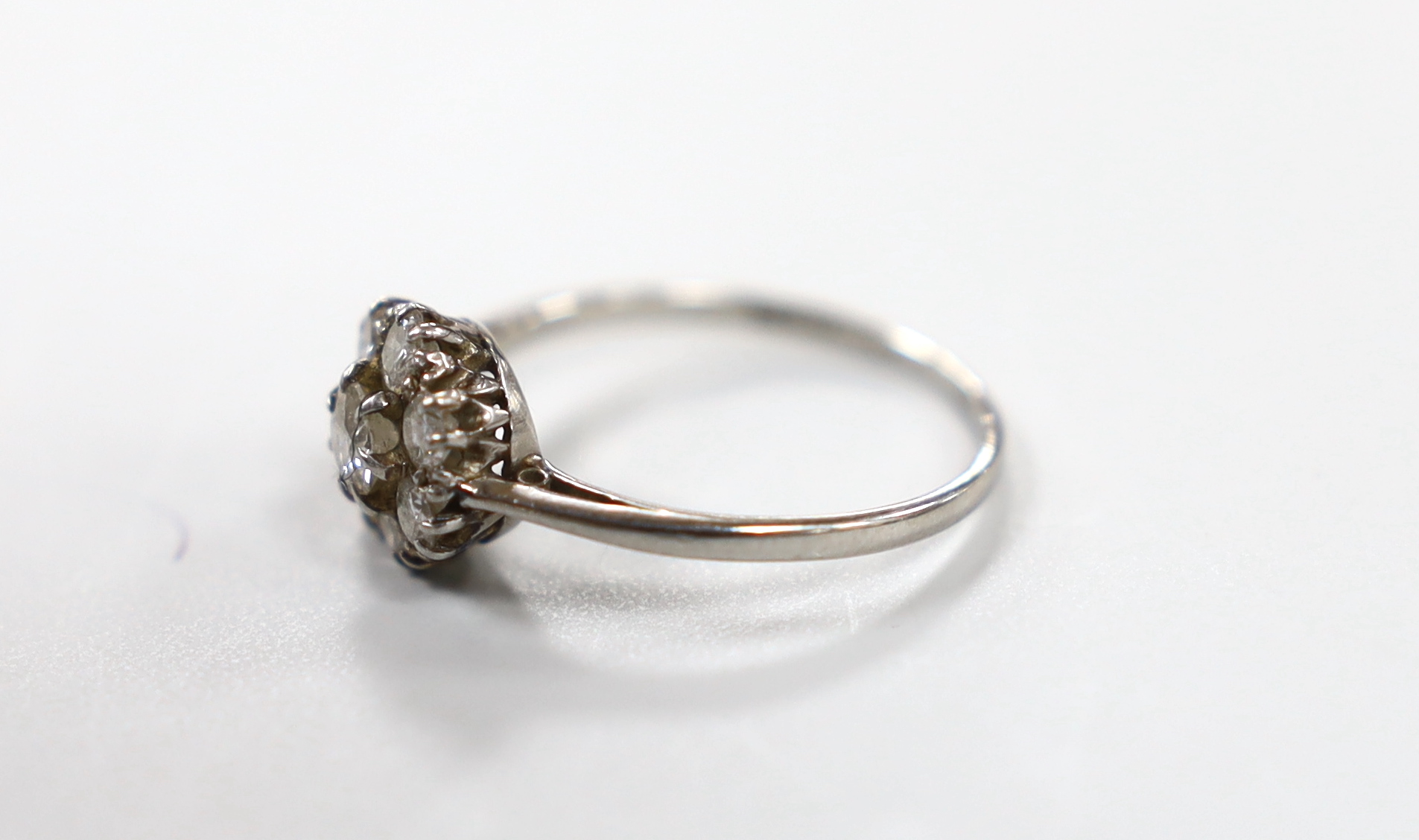 A white metal (stamped platinum) and eight stone diamond set flower head cluster ring, size M/N, gross weight 2.7 grams, (a.f.).